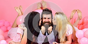 Man with beard and mustache attracts blonde and brunette girls. Girls fall in love with macho, kissing, pink background