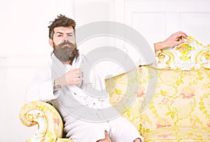 Man with beard and mustache enjoys morning while sitting on luxury sofa. Elite leisure concept. Man on sleepy face in