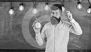 Man with beard and mustache on forgetful face itching head. Bearded hipster holds clock, chalkboard on background, copy