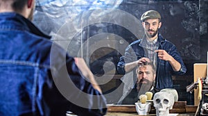 Man with beard and mustache in hairdressers chair in front of mirror background. Reflexion of barber styling hair of