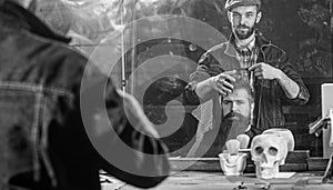 Man with beard and mustache in hairdressers chair in front of mirror background. Reflexion of barber styling hair of