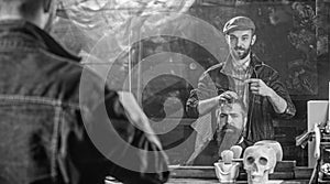 Man with beard and mustache in hairdressers chair in front of mirror background. Reflexion of barber styling hair of