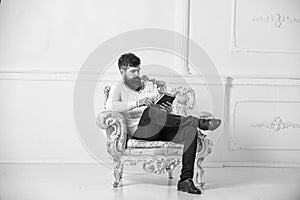 Man with beard and mustache sits on armchair and reading, white wall background. Connoisseur of literature concept