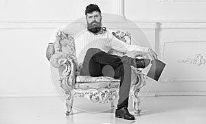 Man with beard and mustache sits on armchair and reading, white wall background. Connoisseur, professor enjoy literature