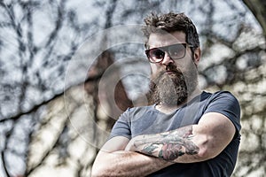 Man with beard and mustache on strict face, nature background, defocused. Bearded man wears stylish sunglasses. Hipster