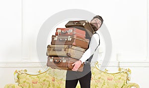 Man with beard and mustache wearing classic suit delivers luggage, luxury white interior background. Butler and service