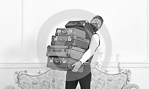 Man with beard and mustache wearing classic suit delivers luggage, luxury white interior background. Butler and service