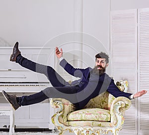 Man with beard and mustache wearing fashionable classic suit, sits, jumps on old fashioned armchair. Macho attractive
