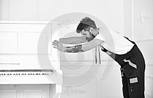 Man with beard and mustache, worker in overalls pushes piano, white background. Delivery service concept. Loader moves