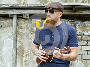 Man with beard playing ukulele and smoking a pipe