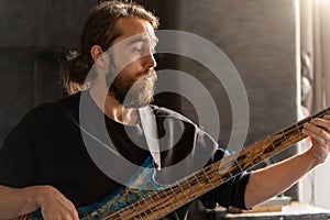 Man with beard plays bass guitar. His fingers move quickly along the strings, creating music. Musician focused and in