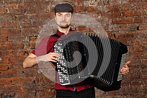 Man with beard plays on bayan, wearing hat in photo