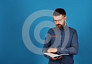 Man with beard reads blue book on blue background.