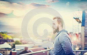 Man with a beard and short hair, in a gray jacket, standing on the background of the urban landscape with clouds setting sun