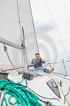 Man sits on sailing yacht and looks through binoculars
