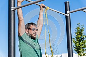 man with beard and sunglasses training his back by doing pull-ups on a bar in an outdoor gym