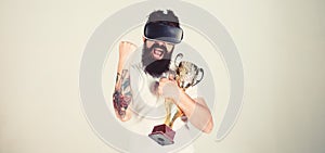 Man with beard in virtual reality glasses holds goblet, light background. Hipster on happy face squeezing fist as