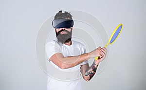 Man with beard in VR glasses beating pitch, grey background. Virtual sport concept. Guy with VR glasses play tennis with