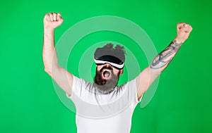 Man with beard in VR glasses, green background. Hipster on shouting face raising hands powerfully while interact in