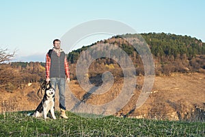 A man with a beard walking his dog in the nature, standing with a backlight at the rising sun, casting a warm glow and
