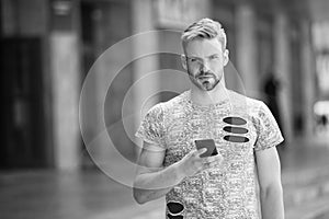 Man with beard walks with smartphone urban background. Guy use smartphone to send message or find location. Man use