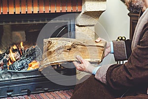 Man with beard wearing bathrobe puts log in burning fireplace