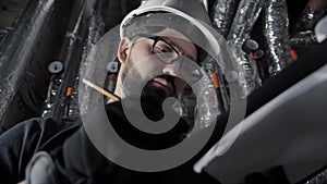 Man with beard, wearing white helmet stands in a boiler room, inspects