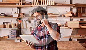 Man with beard in woodwork studio using phone and tablet