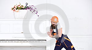 Man with beard worker in helmet and overalls pushes, efforts to move piano, white background. Heavy loads concept