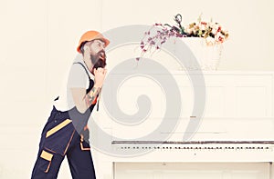 Man with beard, worker in overalls and helmet pushes piano, white background. Delivery service concept. Loader moves