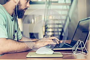 Man with a beard is working at the computer, on the background two floors of apartments