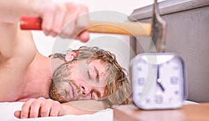 Man bearded annoyed sleepy face lay pillow near alarm clock. Guy knocking with hammer alarm clock ringing. Break