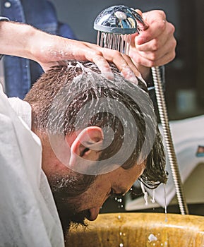 Man bearded client of hipster barbershop. Barbers hands washing hair of bearded hipster. Barbershop concept. Man with