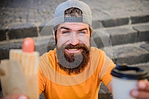 Man bearded eat tasty sausage and drink paper cup. Urban lifestyle nutrition. Junk food. Carefree hipster eat junk food