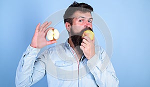 Man bearded eats fruit, holds apple blue background. Half of apple healthy lifestyle. Nutritional value concept