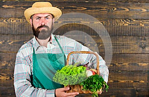 Man bearded farmer presenting eco vegetables wooden background. Farmer straw hat deliver fresh vegetables. Farm delivery