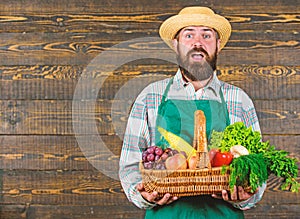 Man bearded farmer presenting eco vegetables wooden background. Fresh organic vegetables in wicker basket. Farmer straw