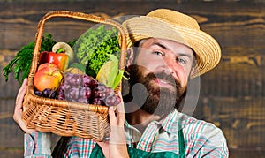 Man bearded farmer presenting eco vegetables wooden background. Fresh organic vegetables in wicker basket. Farmer straw