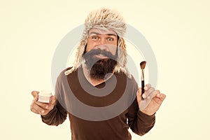 Man bearded fashion stylist wear hat hold brush for applying makeup. Eccentric guy with beard. Makeup and greasepaint