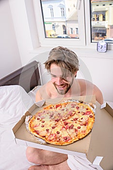 Man bearded handsome bachelor eating cheesy food for breakfast in bed. Man likes pizza for breakfast. Break diet concept