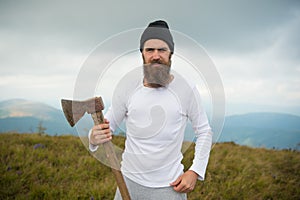 Man bearded hipster with axe stand on mountain landscape
