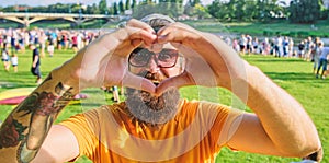 Man bearded hipster in front of crowd people show heart gesture riverside background. Hipster happy celebrate event