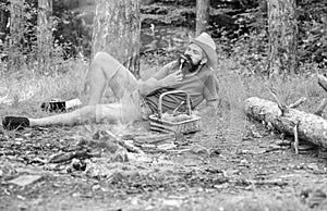 Man bearded hipster lay near campfire after day hiking or gathering mushrooms. Man have snack or picnic in forest. Guy