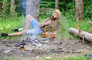 Man bearded hipster lay near campfire after day hiking or gathering mushrooms. Man have snack or picnic in forest. Guy