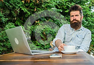 Man bearded hipster make pause for drink coffee and think while sit with laptop. Break to relax. Guy drinks coffee