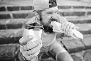 Man bearded shows paper cup drink stairs background. Take coffee with you. Fast food meal for lunch. Hipster bite hot