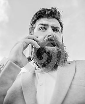 Man bearded surprised businessman hold mobile phone sky background. Hipster smartphone call partner. Man mobile call