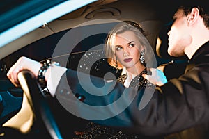 Man and beautiful sensual young woman in formal wear sitting in car