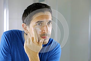 Man beauty applying face cream in home bathroom looking in the mirror. Men skin care concept