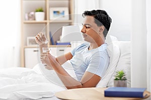 Man in bed dropping medicine into glass of water